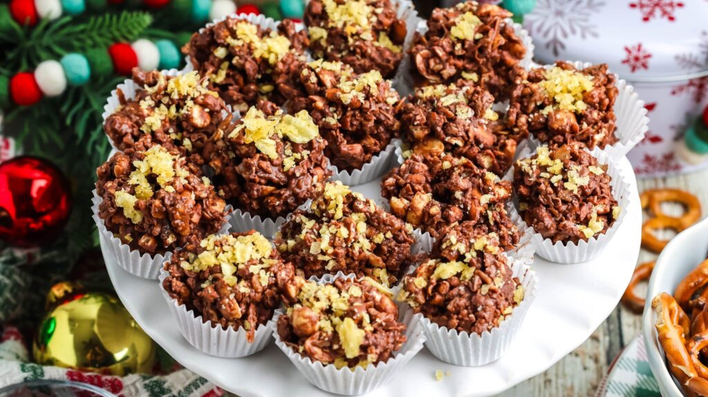 Chocolate potato chip clusters topped with crushed chips on a white cake stand with festive Christmas decorations.